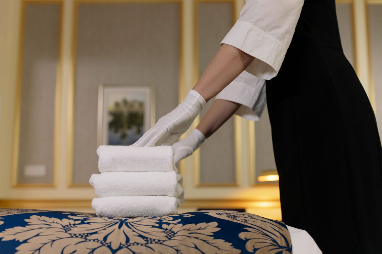 heros-img Une femme de chambre d’hôtel empile soigneusement des serviettes propres dans un décor de chambre luxueux.